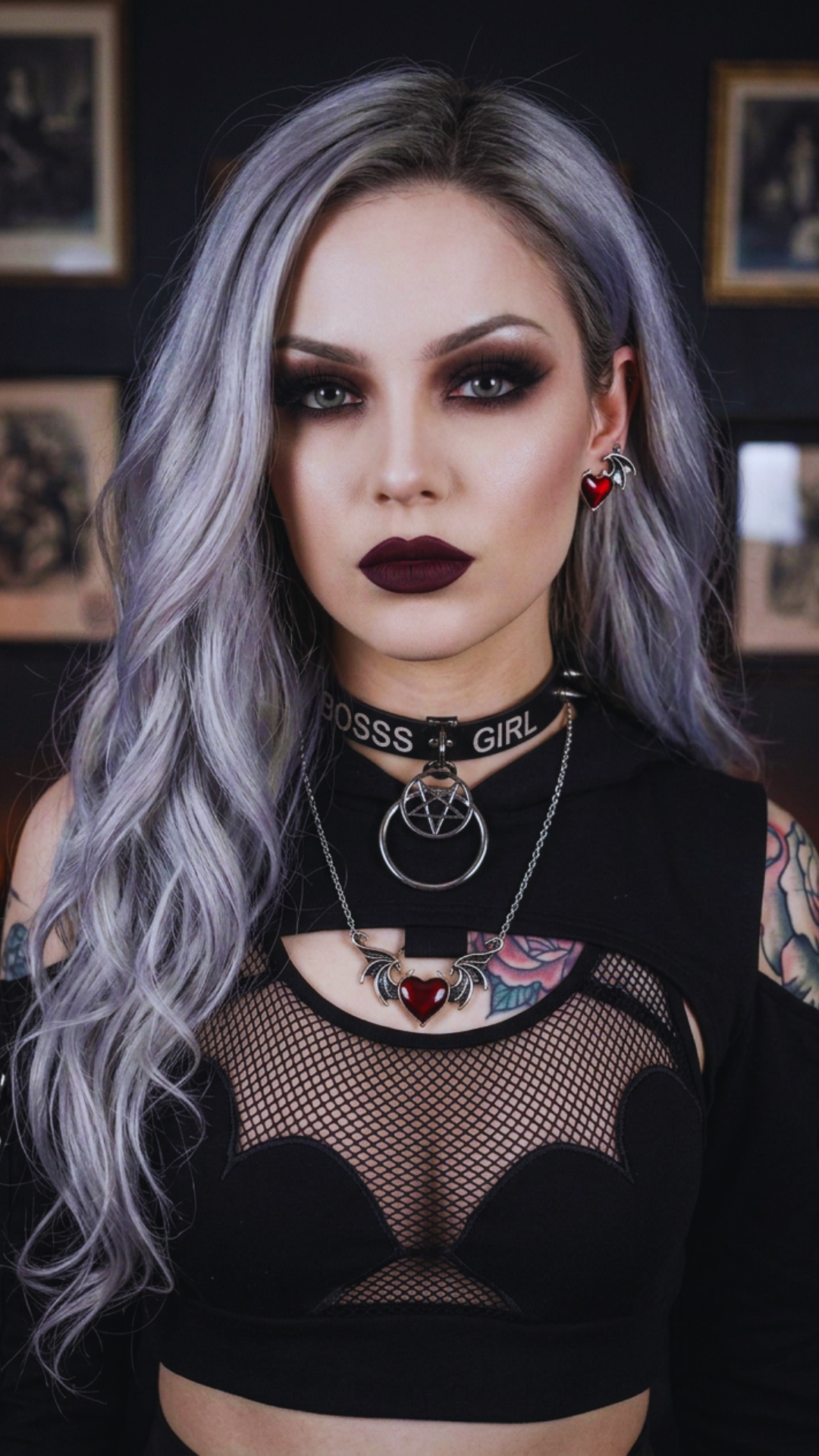 Gothic red heart bat wing earrings and matching necklace worn by goth model with silver-gray hair, smoky eye makeup, and dark burgundy lips, styled in black fishnet crop top with choker in moody tattoo parlor setting — Shadow Realm Supply