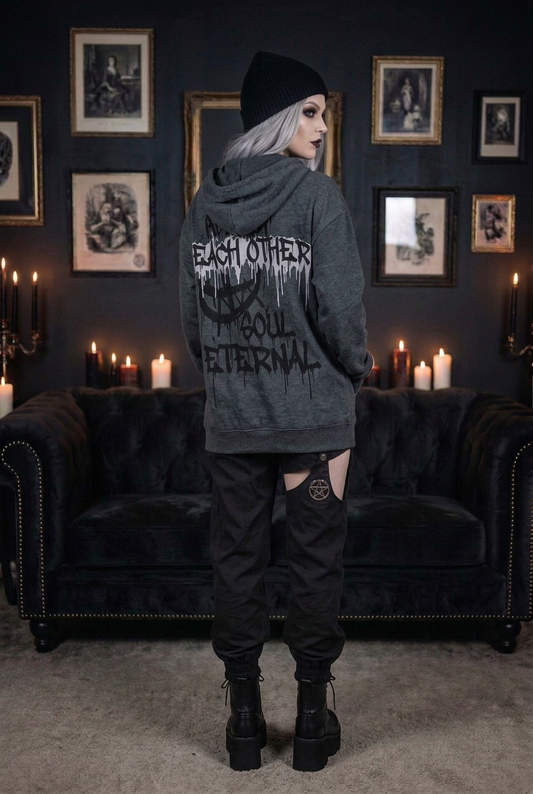 Oversized dark gray gothic hoodie with 'Each Other Soul Eternal' drip text graphic print on back, worn by goth model with black beanie and platform combat boots, back view in candlelit gothic interior — Shadow Realm Supply