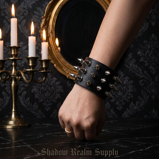 Wide black leather punk spike bracelet with silver rivets worn on wrist in gothic manor with candles and ornate mirror — Shadow Realm Supply