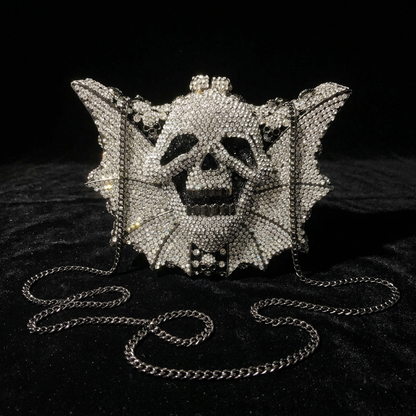 Crystal rhinestone skull bat wing clutch evening bag with silver chain strap, front view on black velvet surface — gothic alt fashion statement bag — Shadow Realm Supply