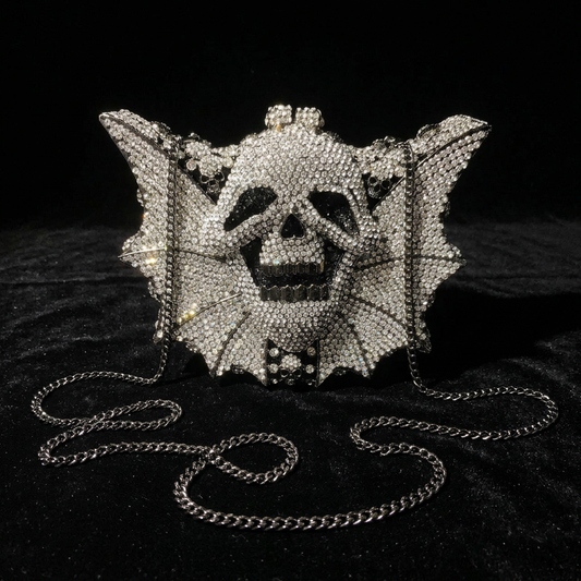 Crystal rhinestone skull bat wing clutch evening bag with silver chain strap, front view on black velvet surface — gothic alt fashion statement bag — Shadow Realm Supply