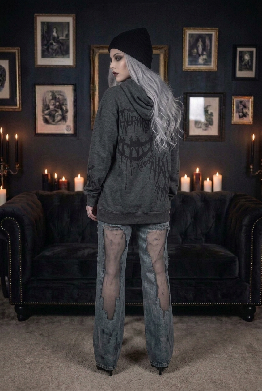 Goth model with silver-gray hair wearing oversized dark gray gothic drip graphic hoodie with black beanie and heavily destroyed mesh fishnet flare jeans with stiletto heels, back view showing full hoodie graphic and jean destruction detail in candlelit gothic interior — dark aesthetic alt grunge streetwear outfit — Shadow Realm Supply