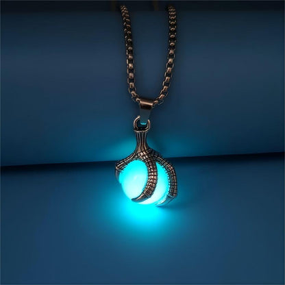 Glow in the dark dragon claw pendant necklace with teal glowing orb on antique bronze box chain, displayed on dark blue surface — gothic witchy alt fashion jewelry — Shadow Realm Supply