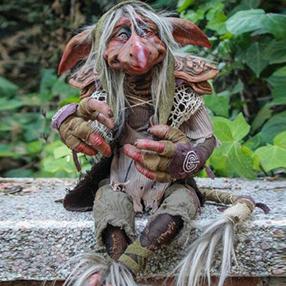 Gothic goblin sculpture with white beard and ragged clothes sitting on stone ledge in forest setting