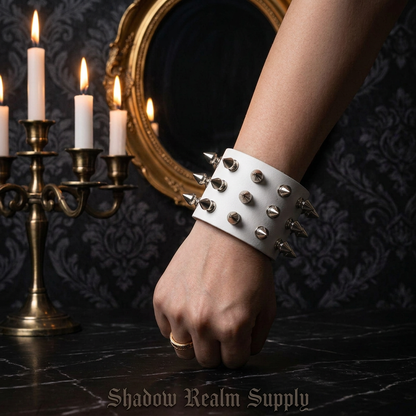 Wide white leather punk spike bracelet with silver rivets worn on wrist in gothic manor with candles and ornate mirror — Shadow Realm Supply