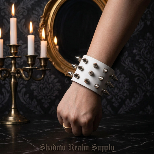 Wide white leather punk spike bracelet with silver rivets worn on wrist in gothic manor with candles and ornate mirror — Shadow Realm Supply