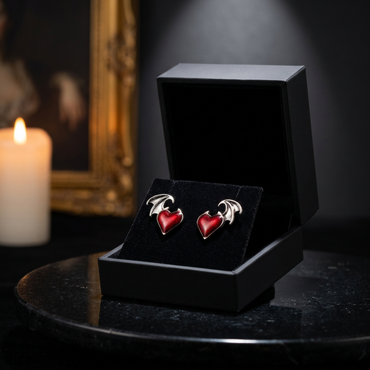 Gothic red enamel heart with silver bat wing stud earrings displayed in open black velvet gift box on marble surface, candlelit gothic interior — Shadow Realm Supply